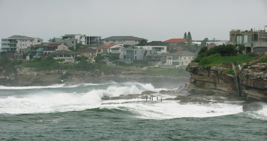 Waves crash into the cliffs beneath a city on a cloudy day