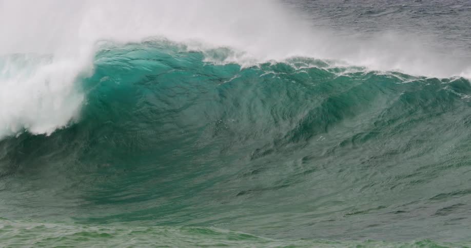 A big wave with ocean foam breaks on the shore