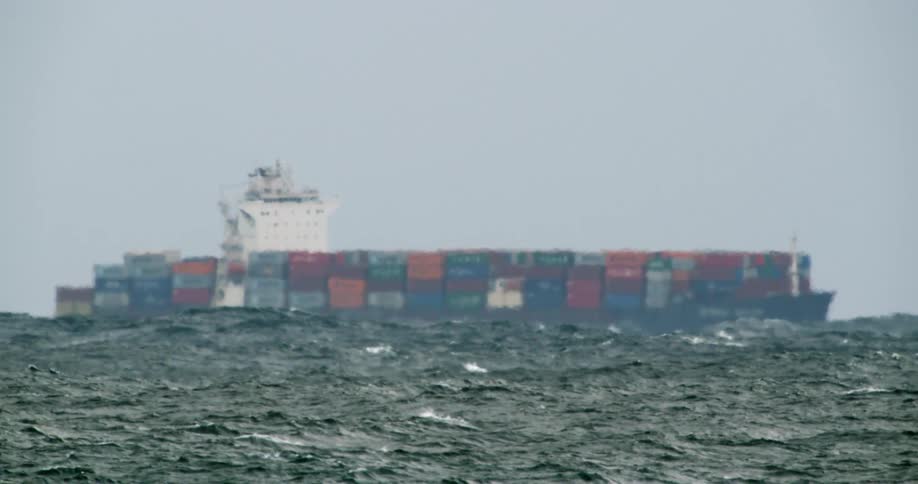 A cargo ship fulling of shipping containers moves across a choppy sea