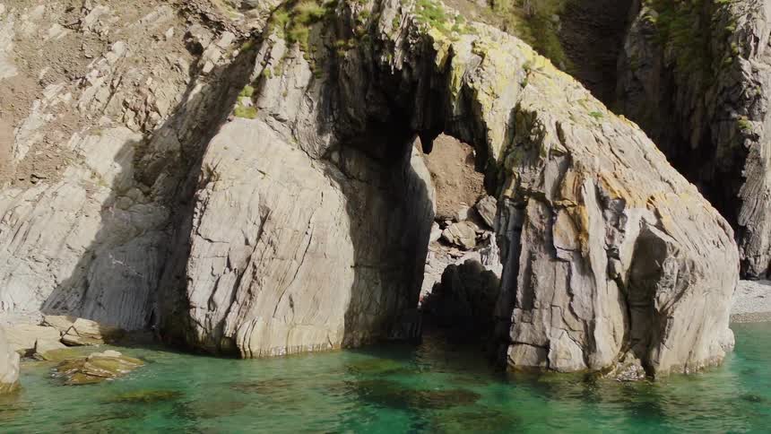 Aerial view of a natural arch rising from the coast on the green sea waters