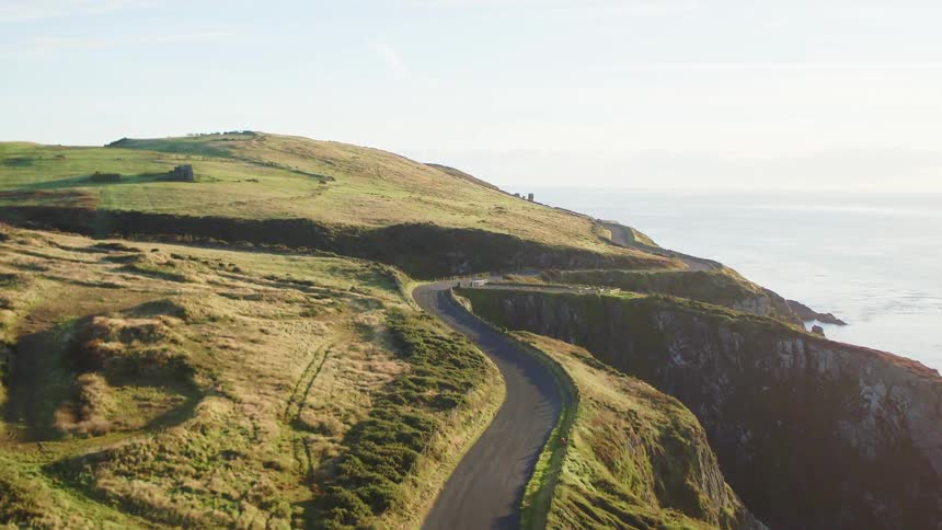 A curvy road running along the cliffs of a hilly countryside bordering the ocean