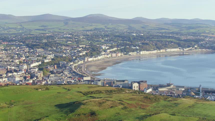 Wall forms barrier on shore for city surrounded by mountains and green hills