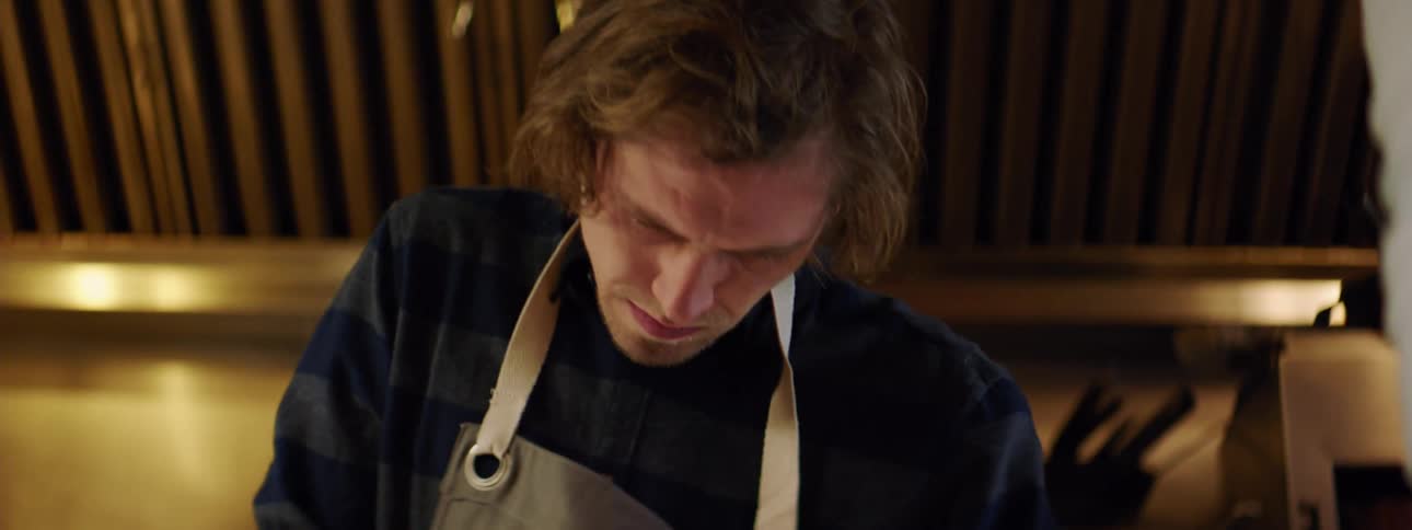 Man in apron works on something off screen
