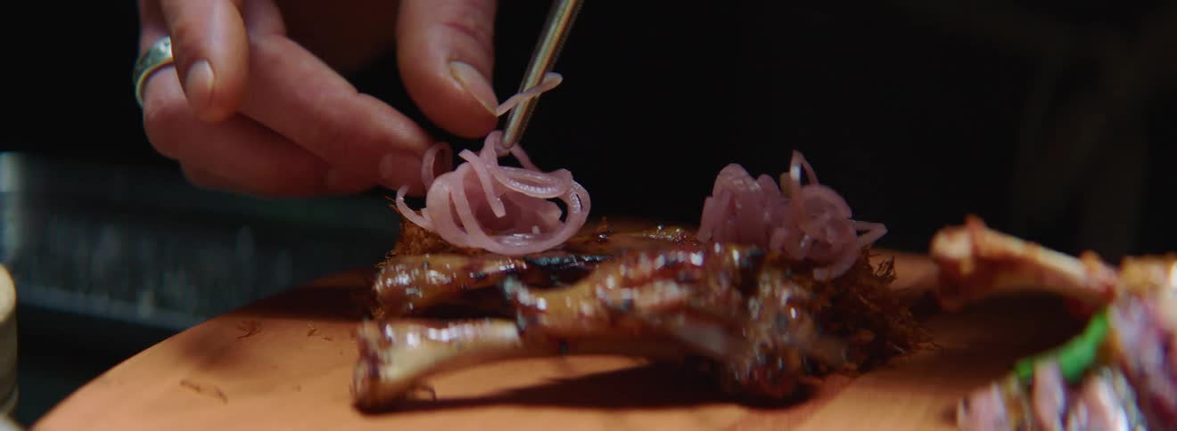 Using kitchen tongs to place dressing on meat on the bone on a wooden platter