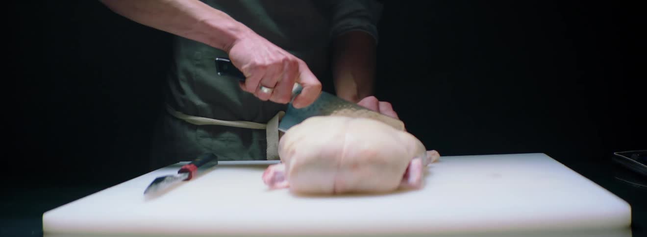 A man picks up a large cleaver and cuts off a piece of raw meat and bone