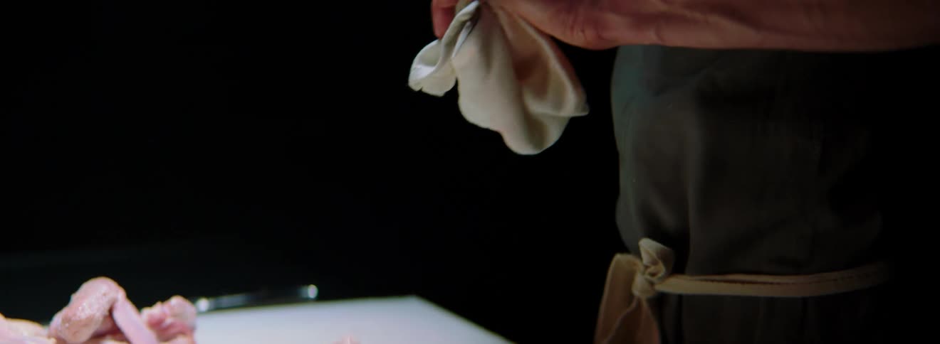 A chef cleans a knife with a rag while cutting meat