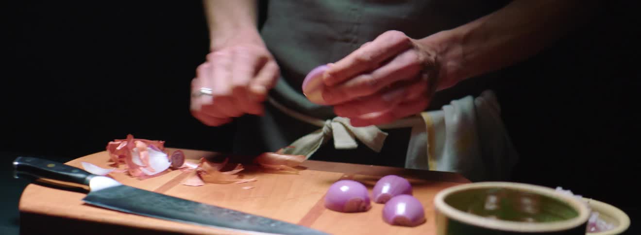 A chef peels the skin off the last shallot half then cleans all the skins off the cutting board