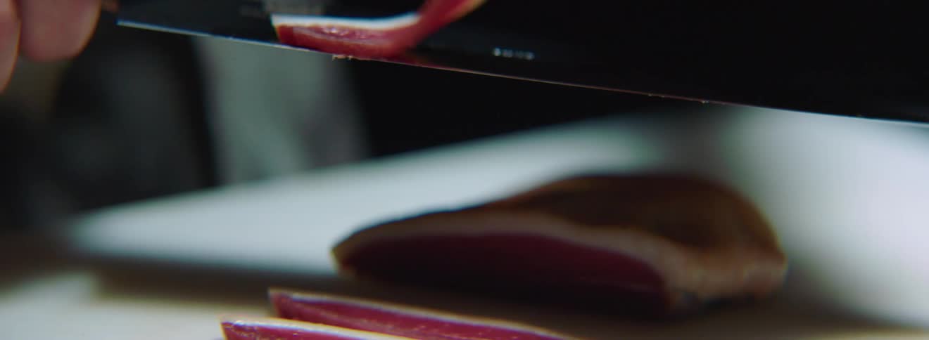 A chef cuts thin slices of duck meat with a large knife