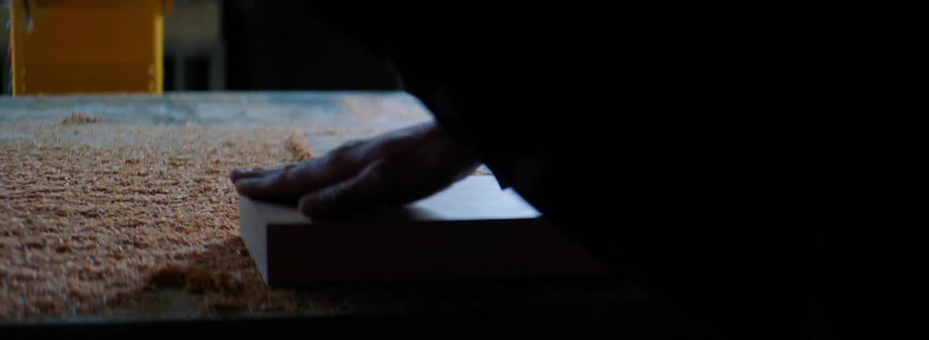 A person stroking a block of wood in a room with a blinking light