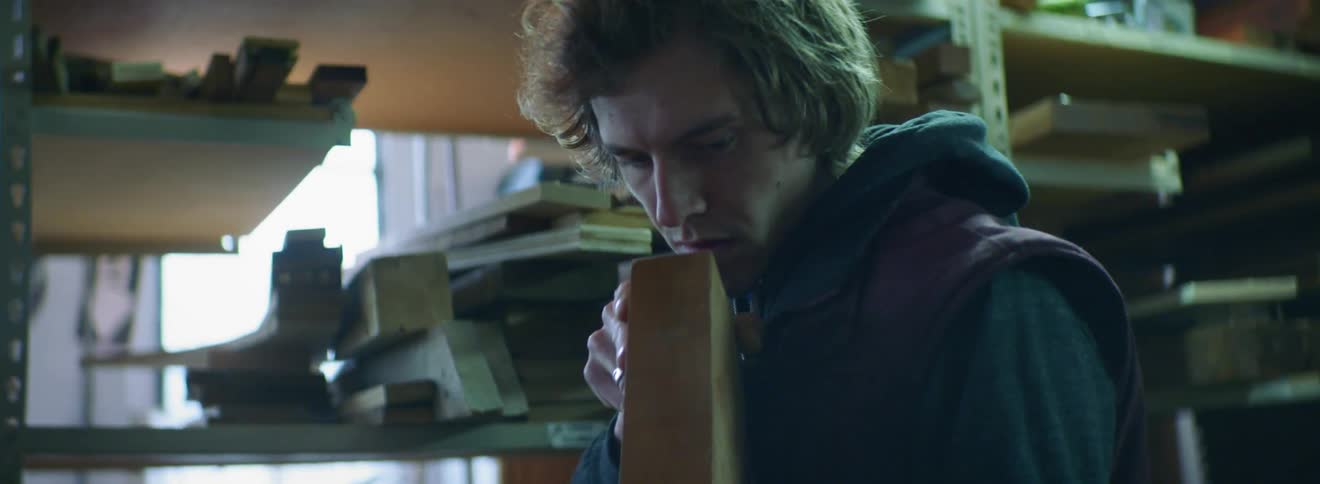 A young man in a workshop inspects a piece of lumber
