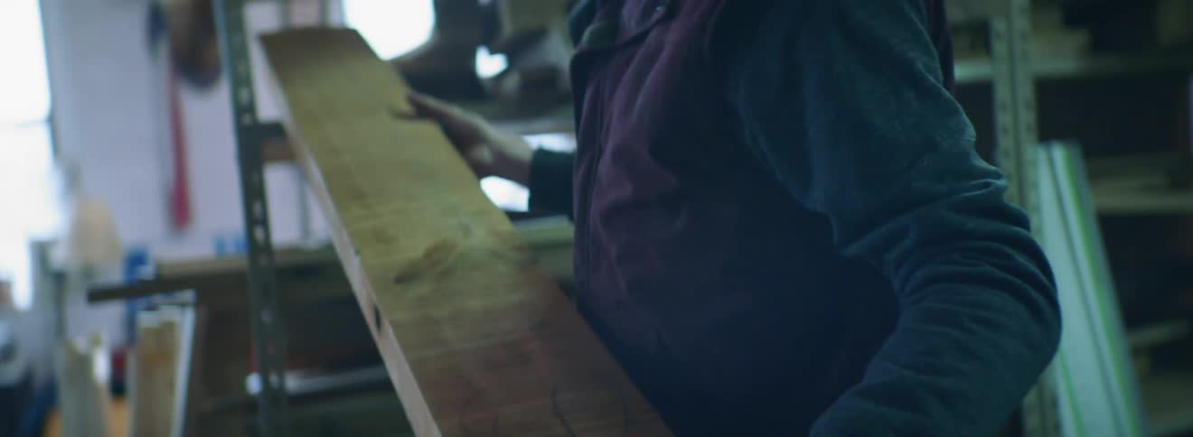 A young man in a workshop removes a piece of lumber from a shelf