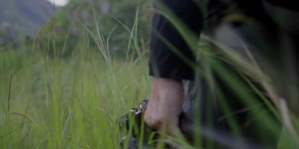 A man is carrying a tripod through a field of tall grass