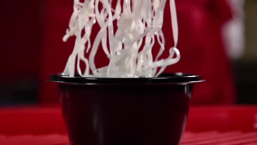 Asian noodles being placed in a black take out plastic bowl