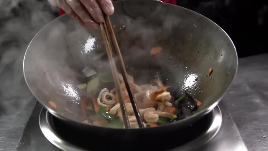 A white person cooks vegetables and meat in a large wok