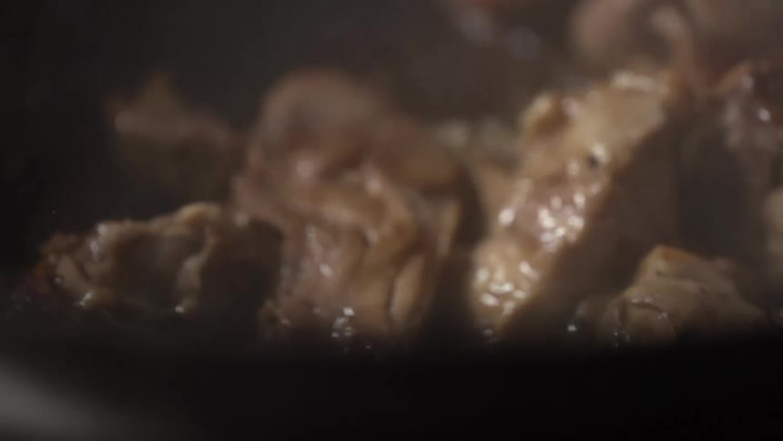 Meat cubes being roasted in a black skillet