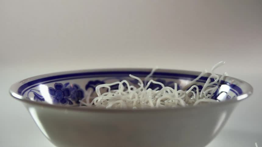 White rice noodles fall into a white ceramic bowl