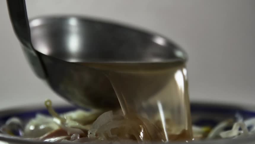 A spoon pouring sauce into a bowl with vegetables