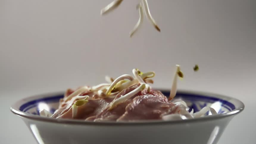 A bowl with food with sprouts falling into the bowl