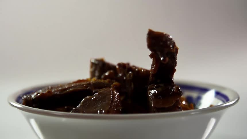 Beef strips drop onto lo mein noodles in blue patterned porcelain bowl