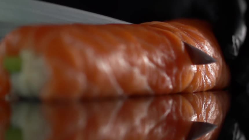 A chef cuts slices from a roll of a sushi