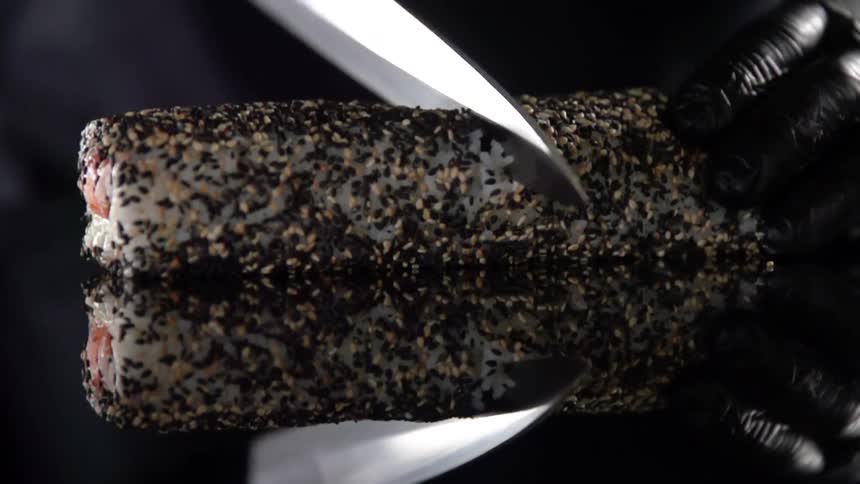 Cook with black gloves cuts sushi with a knife in studio