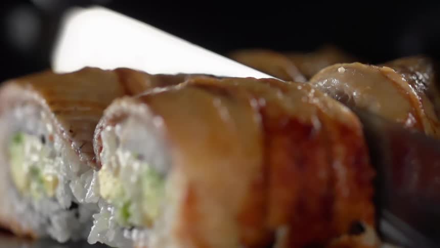 Rolls of sushi being sliced with a sharp kitchen knife
