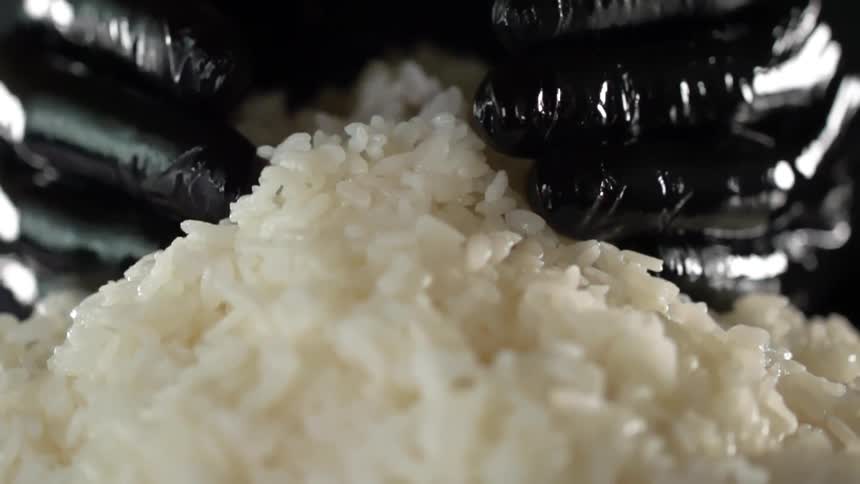 Chef wearing black latex gloves picks up cooked rice from a pile