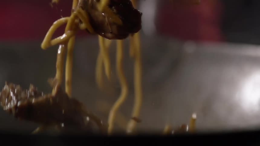 Chow mein with noodles and beef are stirred in a wok