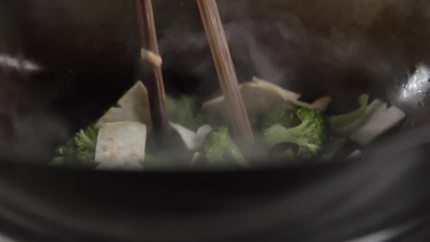 Stirring vegetables with chopsticks inside a steaming hot wok