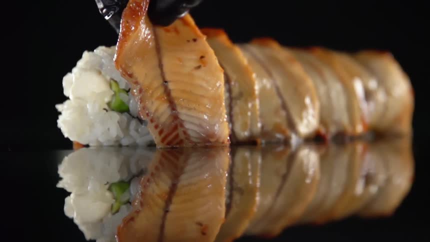 A slice of fish fillet being placed atop vegetables wrapped in rice
