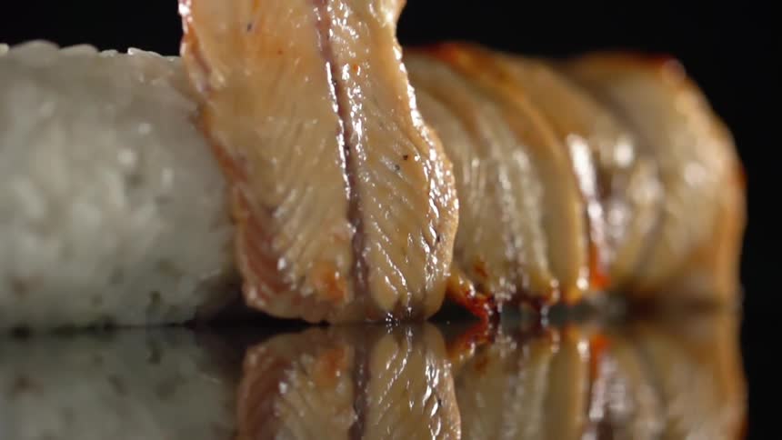 A piece of thinly sliced fish is delicately laid over a sushi roll made of rice
