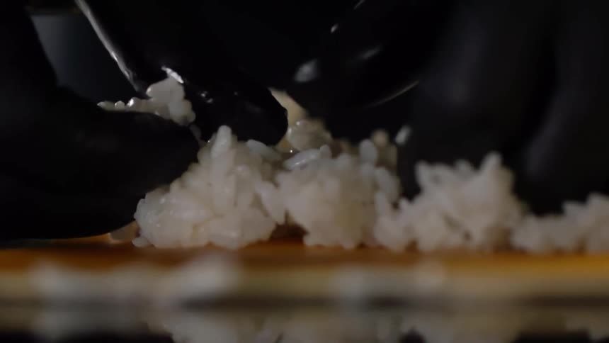 A person wearing black plastic gloves pressing and squeezes clumps of rice