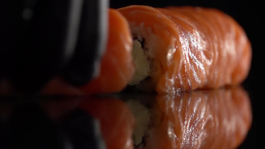 Cook with black gloves cuts sushi in half