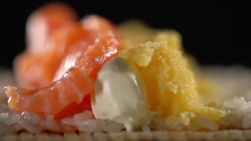 A thin slice of fish and fish roe are piled atop pieces of avocado on rice