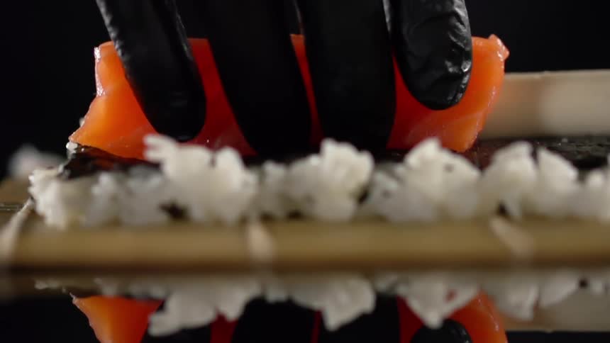 A person with black gloves placing salmon next to rice on a glass table