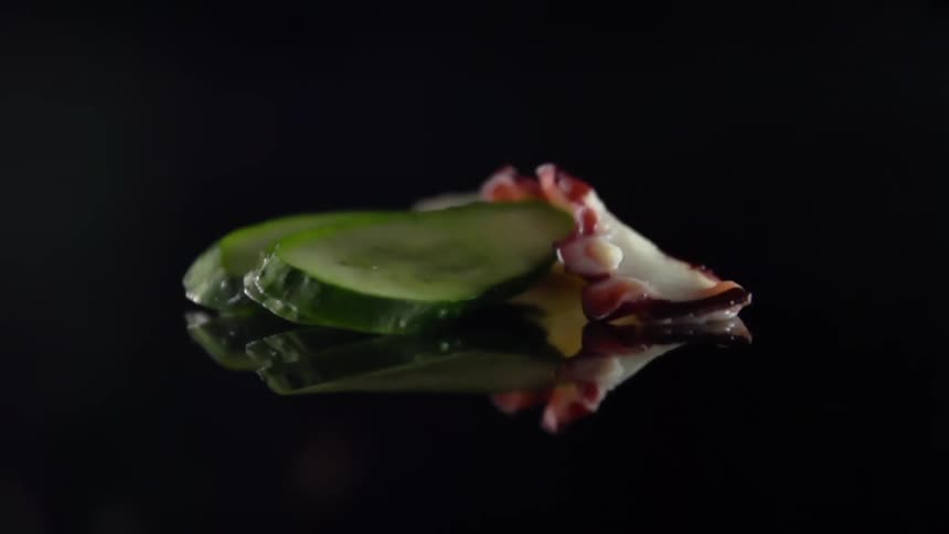 A chef gently lays a piece of eel over slices of pickled cucumber