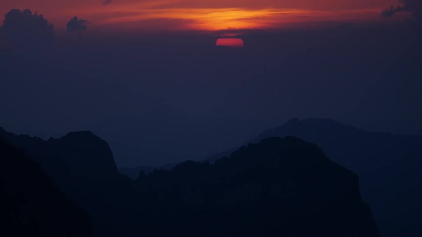 The sun is setting in a cloudy sky