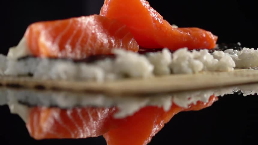 Salmon being placed on top of bamboo and rice on a glass table