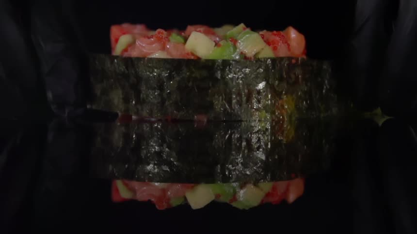 Chef using black latex gloves rolls seaweed around sushi