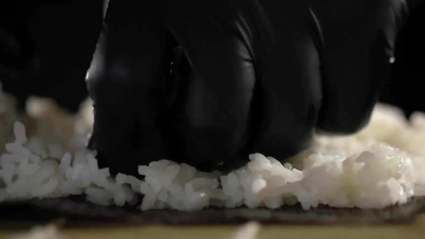 Male cook with black gloves makes a sushi roll