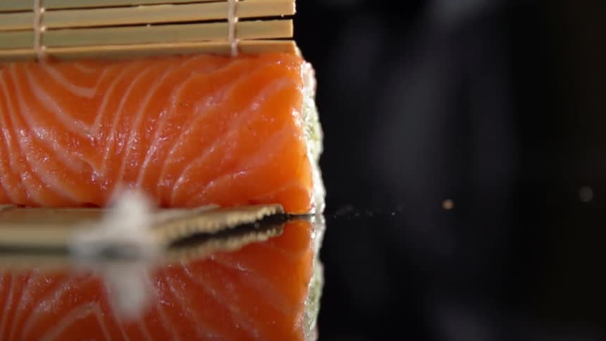 Salmon being wrapped in bamboo on a glass table