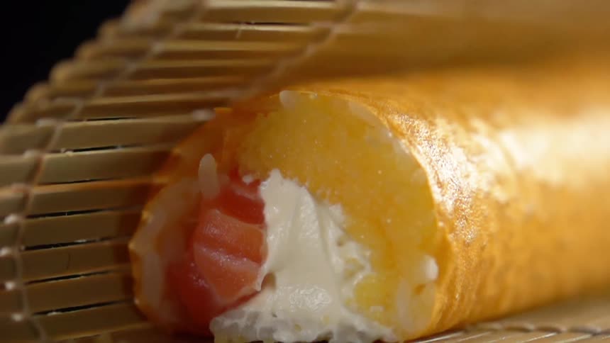 Salmon sushi roll being rolled using a bamboo mat