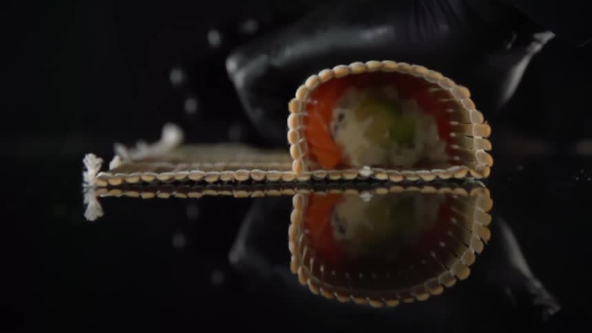 A person using a bamboo sushi rolling mat prepares a delicious looking sushi roll