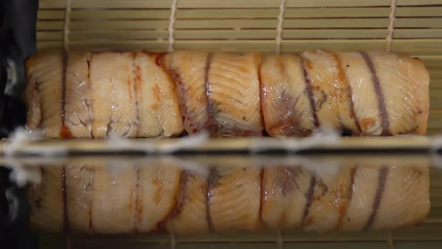 Chef with black latex gloves rolls sushi with a bamboo mat