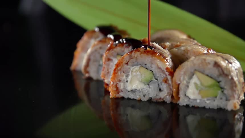 Sauce pouring on sushi rolls over a reflecting surface