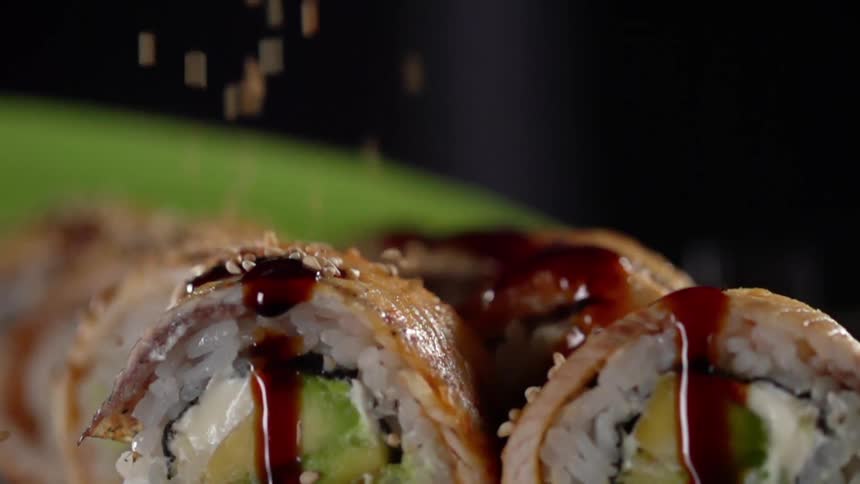 Sesame seeds falling on top of sushi rolls covered in sauce
