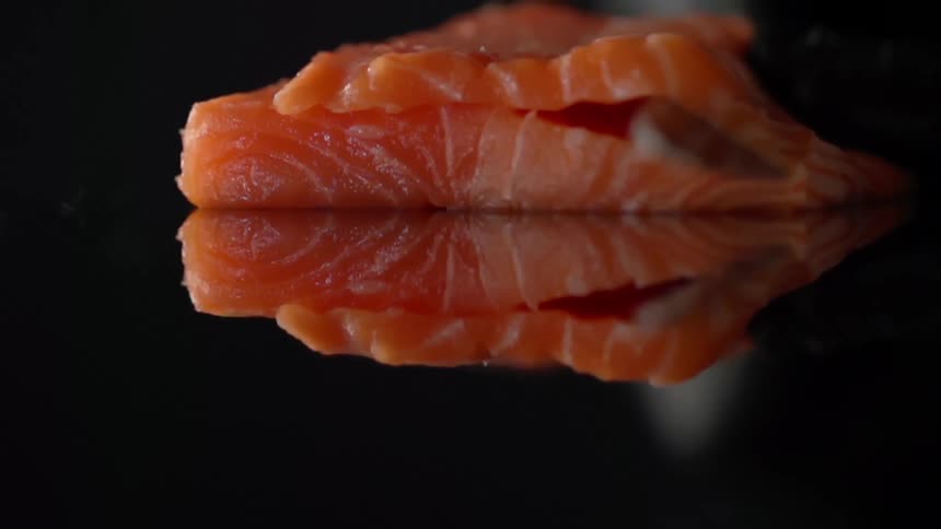 A person with black gloves filleting salmon with a knife on a glass table