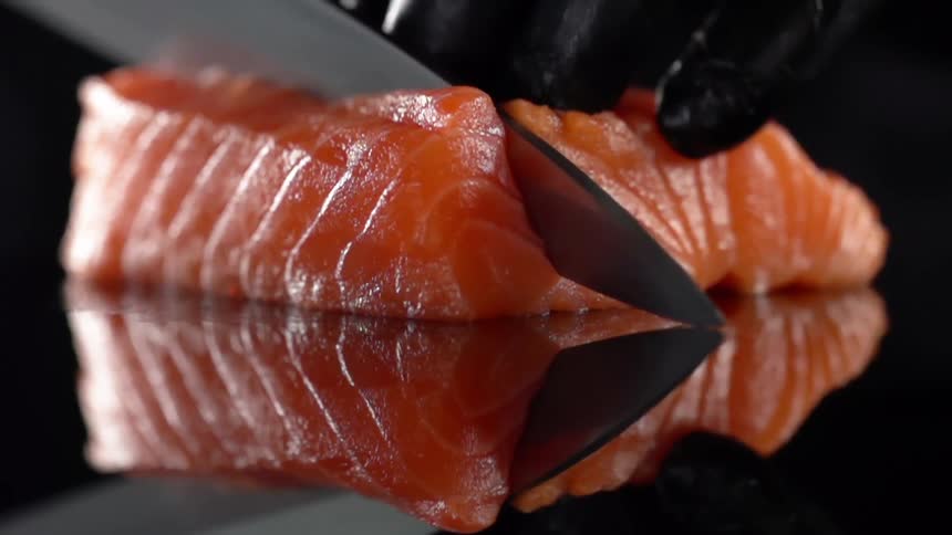 Close up of a cook with black gloves cutting salmon for sushi in studio