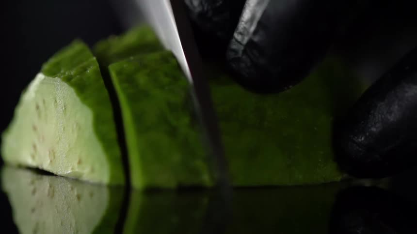 Chef wearing black latex gloves slices a vegetable with a sharp kitchen knife
