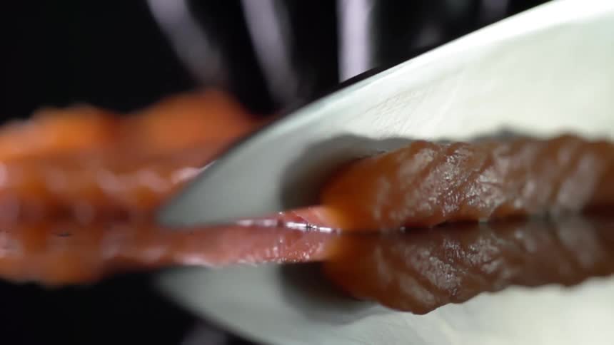 Cook with black gloves cuts salmon with a sharp knife